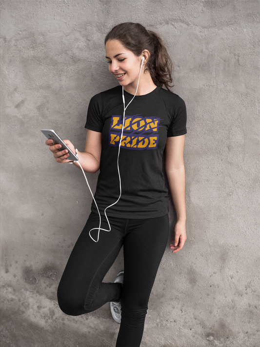 Woman wearing a black t-shirt with 'LION PRIDE' text, using a phone and earphones against a gray concrete wall.