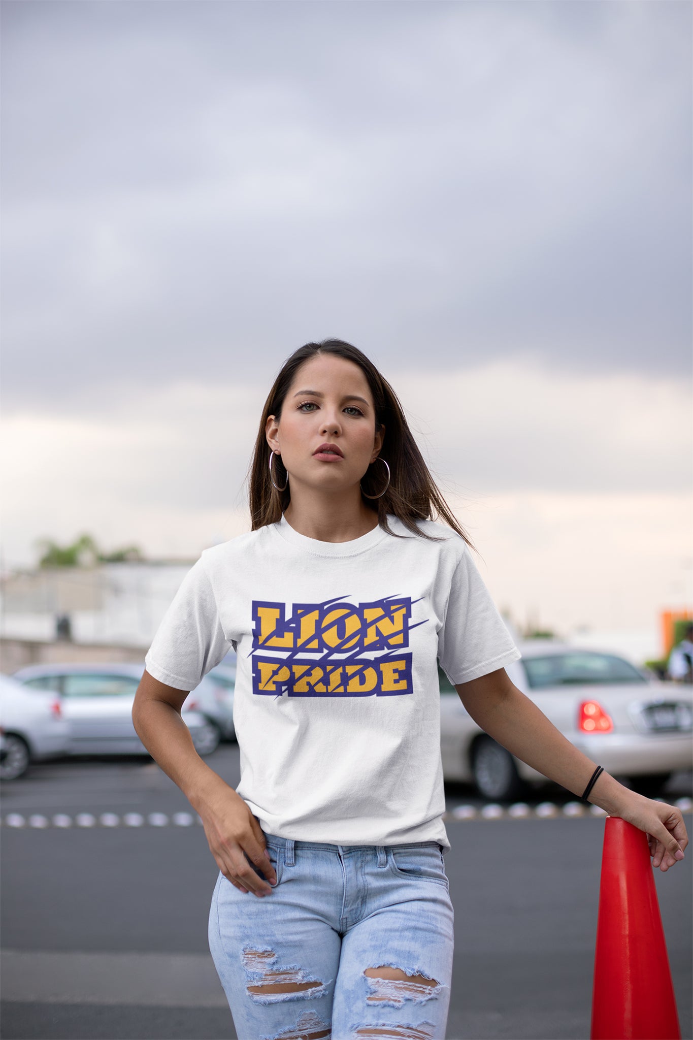 Woman wearing a 'Lion Pride' t-shirt standing outdoors with cars and a red cone in the background.