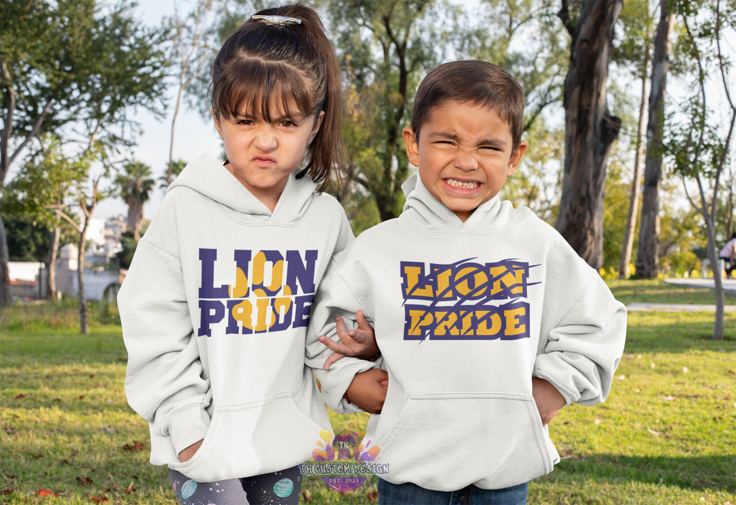 Two children wearing 'Lion Pride' hoodies in a park setting.